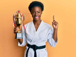 A young martial arts student dressed in gi proudly holding a trophy in the air, signifying the completion a multitude of set goals